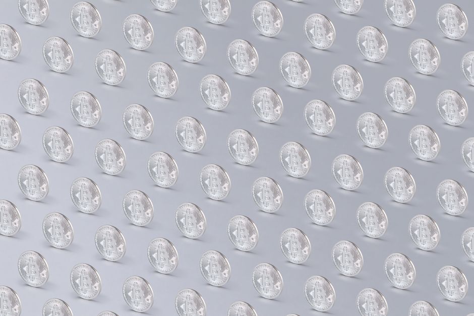 Array of silver Bitcoin coins arranged in a regular pattern over a light background.